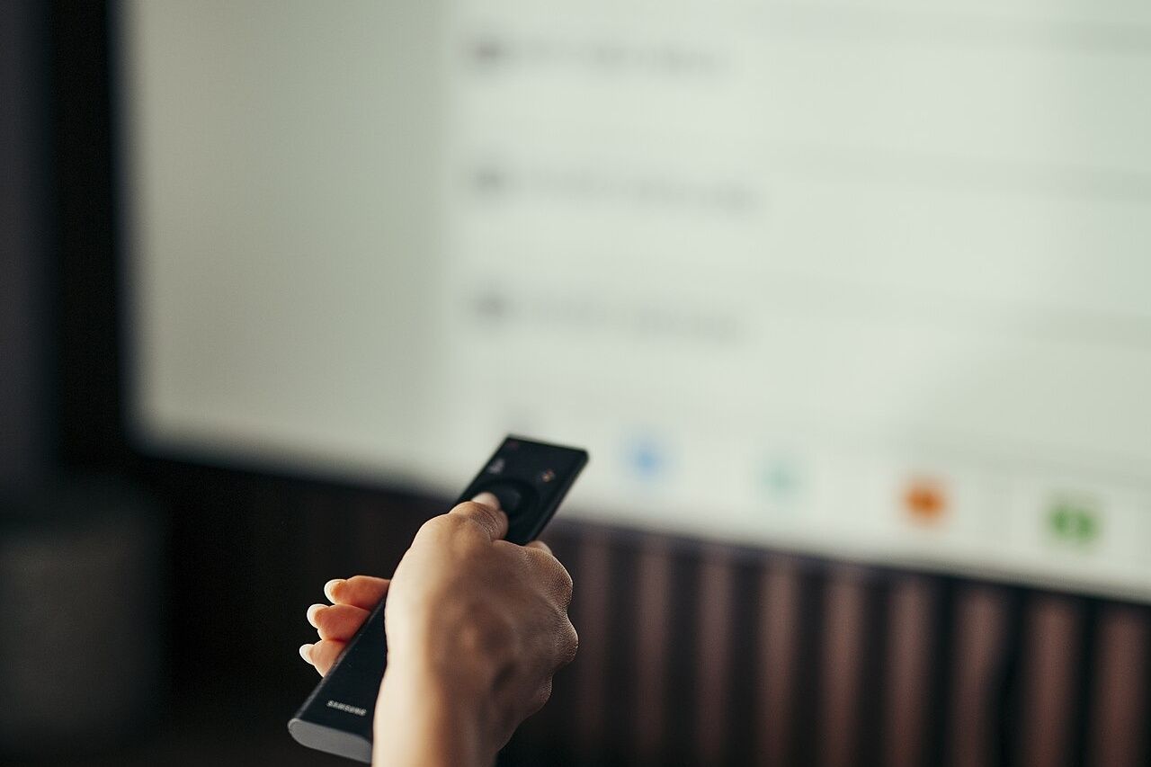 A person sits at home and focuses on the television screen while holding a remot